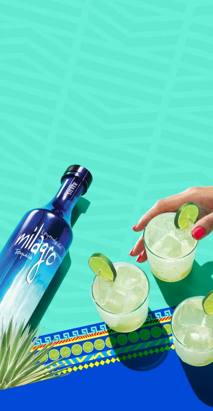 A bottle of Milagro silver tequila with three cocktails